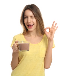 Photo of Young woman with glass cup of chocolate milk showing Ok on white background