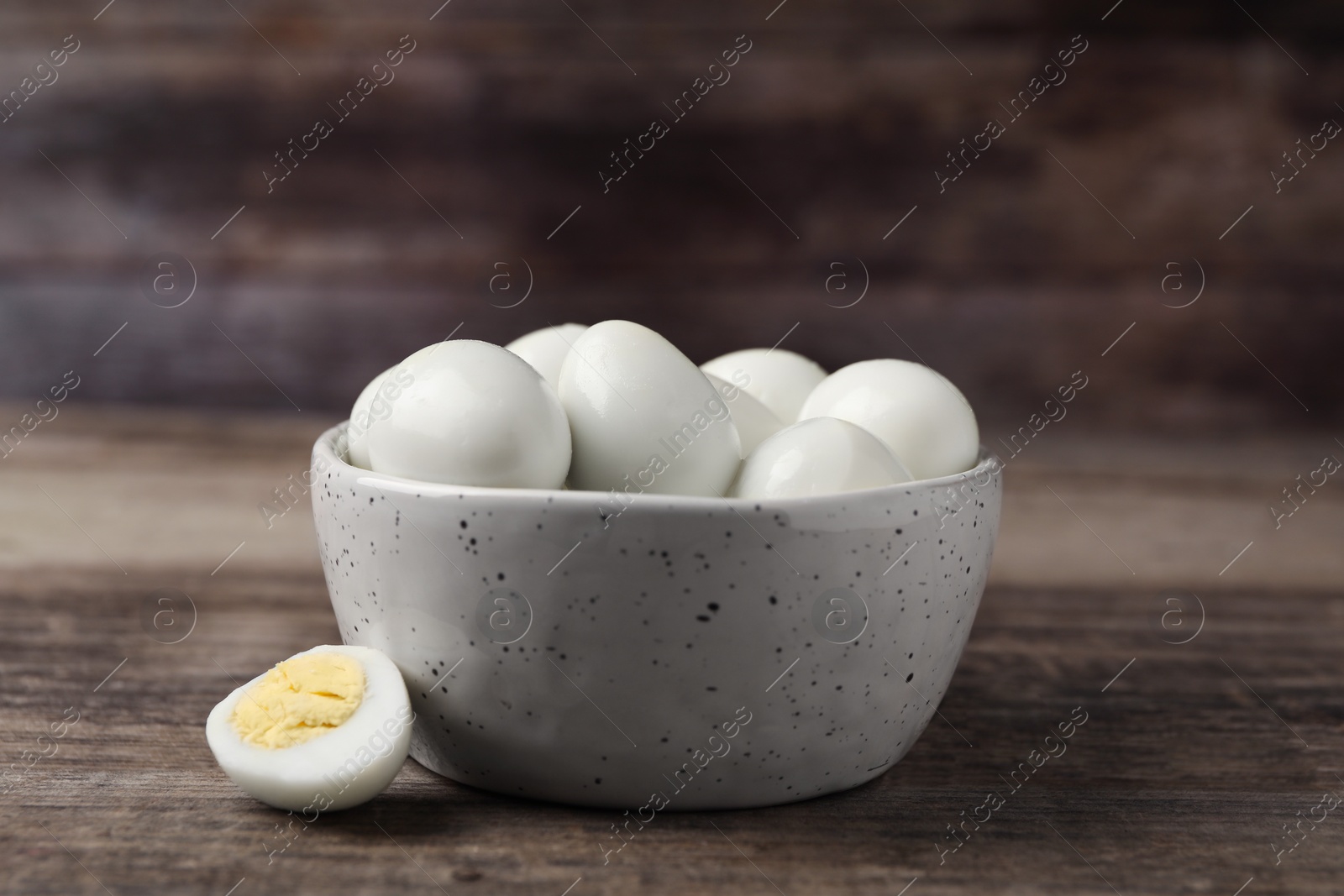 Photo of Many peeled hard boiled quail eggs in bowl on wooden table, closeup