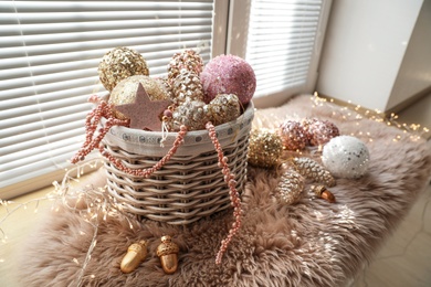 Photo of Basket with beautiful Christmas tree baubles and fairy lights on window sill indoors