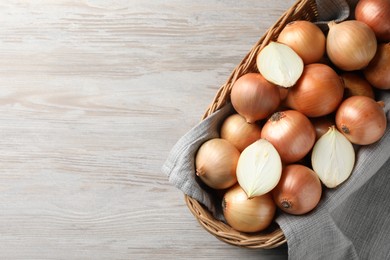 Photo of Wicker basket with whole and cut onions on light grey wooden table, top view. Space for text