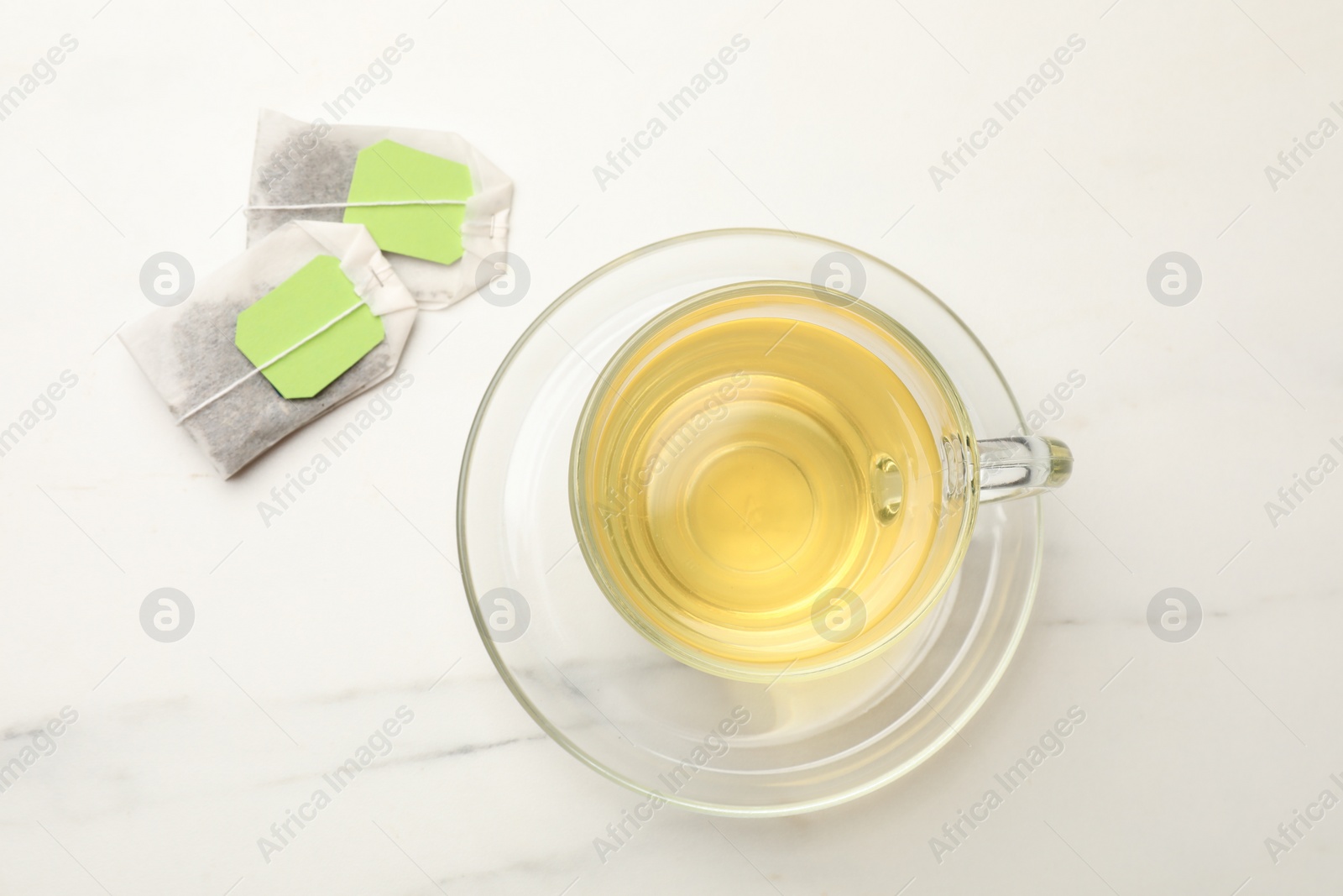 Photo of Tea bags and glass cup of hot beverage on white table, flat lay