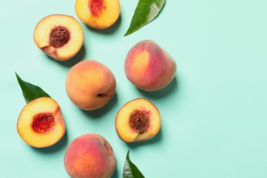 Photo of Cut and whole fresh ripe peaches with green leaves on light blue background, flat lay. Space for text