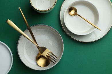 Stylish empty dishware and golden cutlery on green background, flat lay