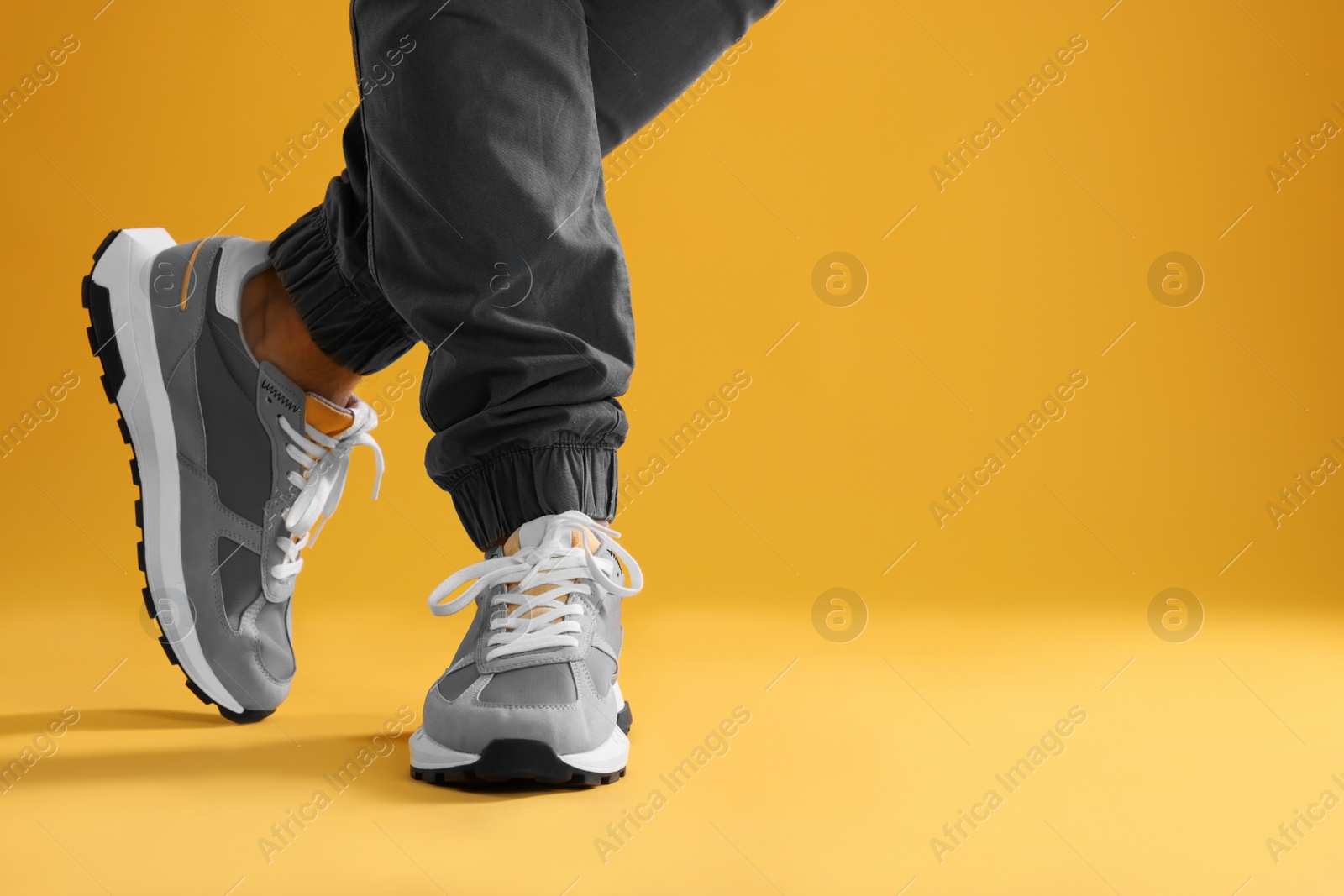 Photo of Man wearing stylish sneakers on yellow background, closeup. Space for text