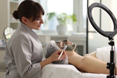 Photo of Cosmetologist applying mask on woman's face in clinic