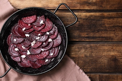 Photo of Roasted beetroot slices with feta cheese in wok pan on wooden table, flat lay. Space for text