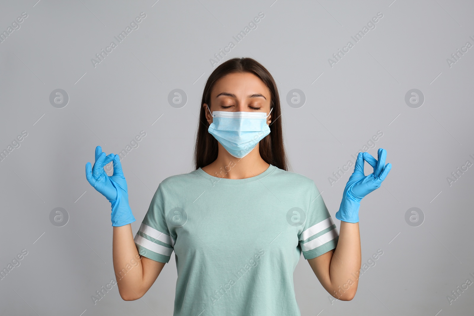 Photo of Woman in protective mask meditating on grey background. Dealing with stress caused by COVID‑19 pandemic