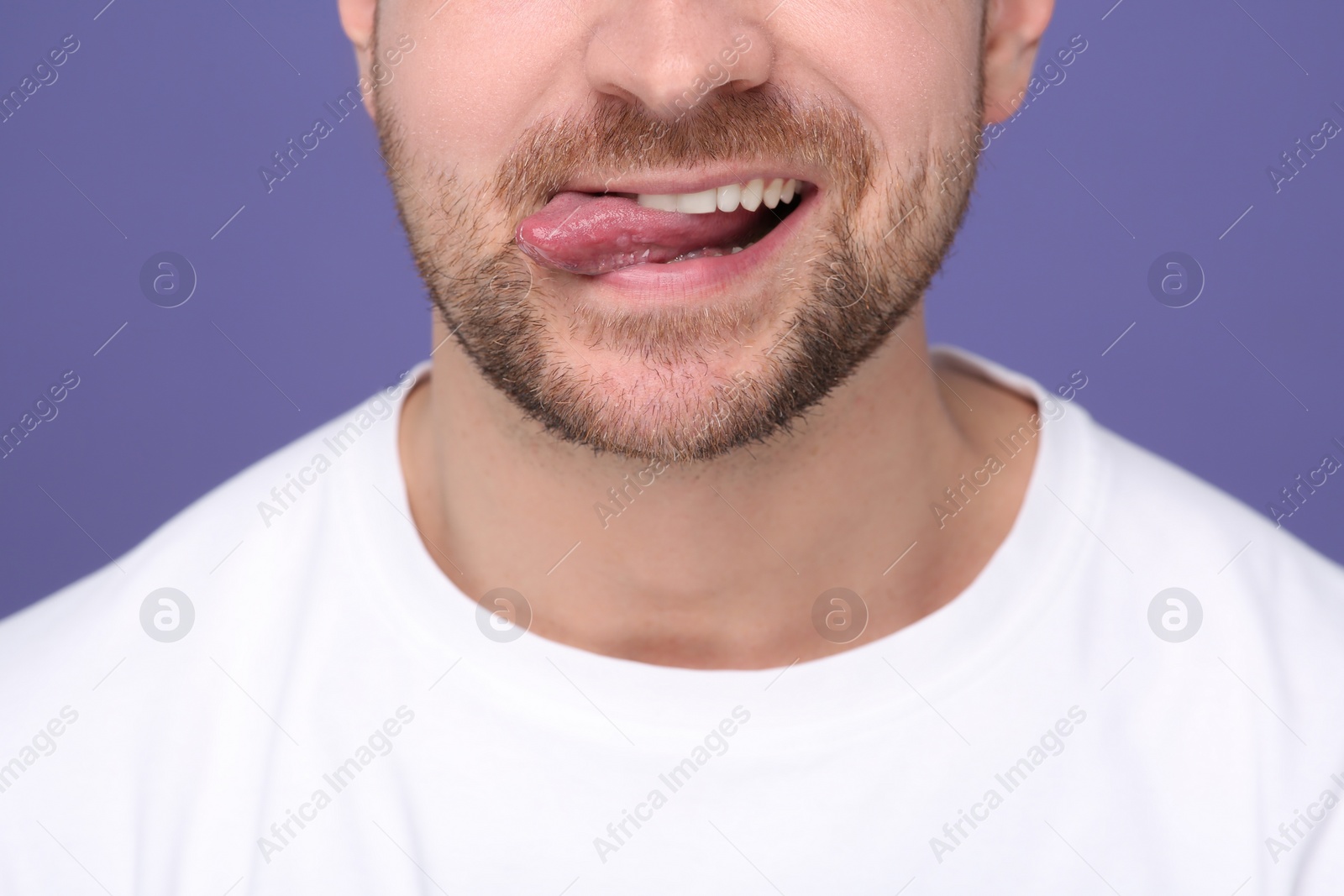 Photo of Man showing his tongue on purple background, closeup