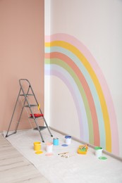 Photo of Different decorator's tools and ladder near wall with painted rainbow indoors