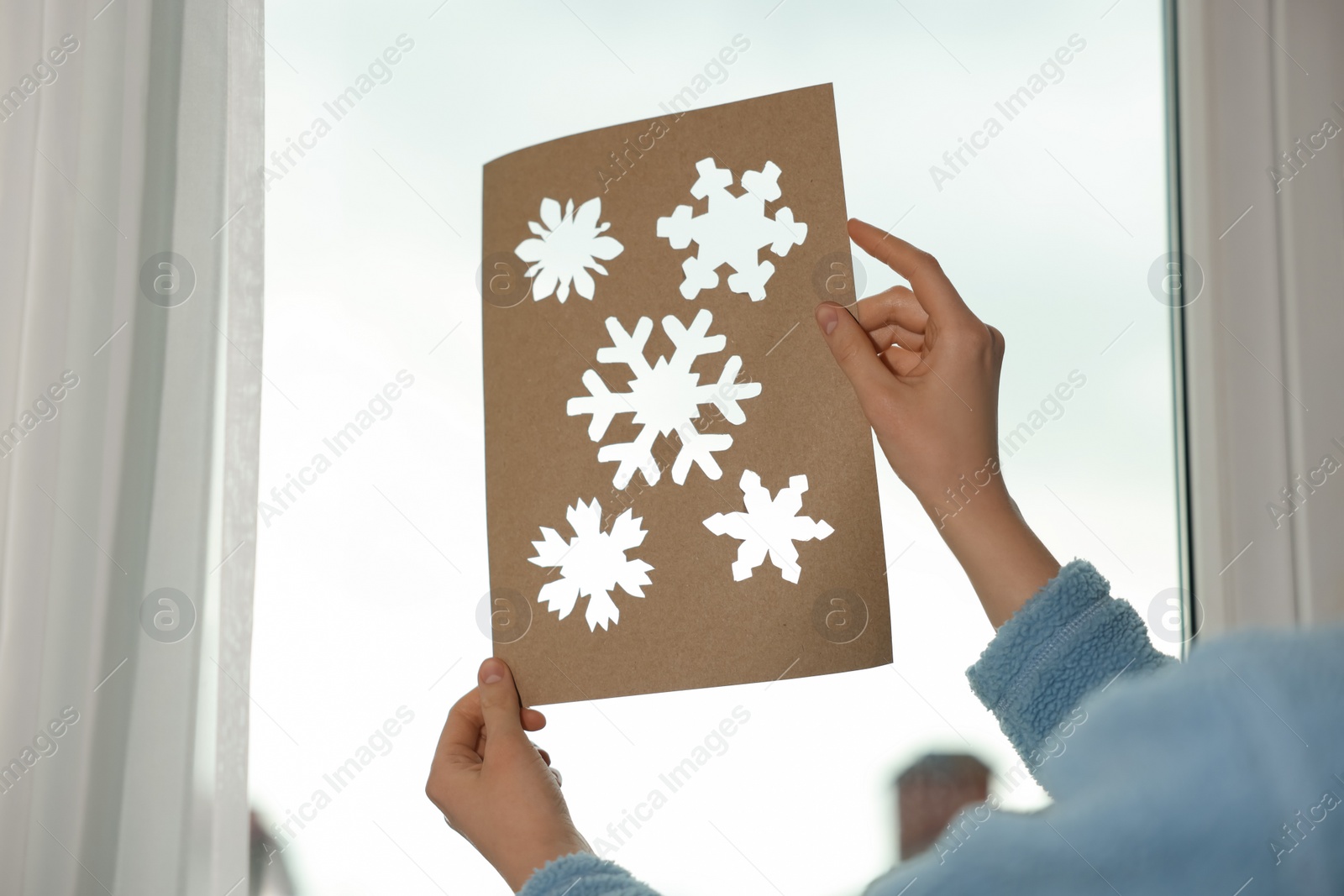 Photo of Woman holding snowflake stencil near window at home, closeup