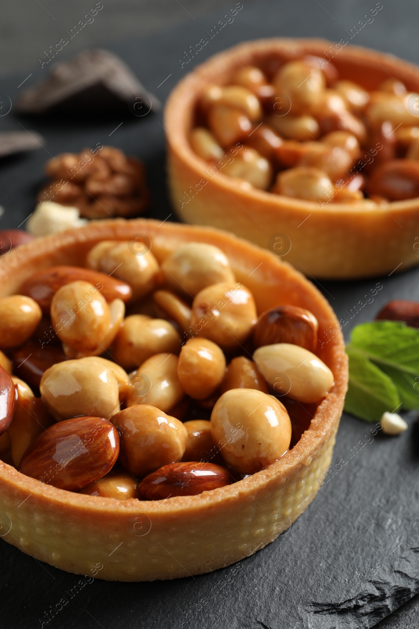 Photo of Tartlets with caramelized nuts on black slate, closeup. Delicious dessert