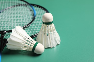Photo of Feather badminton shuttlecocks and rackets on green background, closeup. Space for text