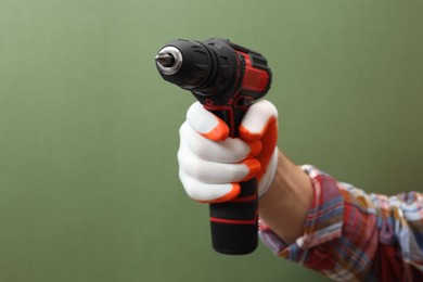 Handyman holding electric screwdriver on pale green background, closeup