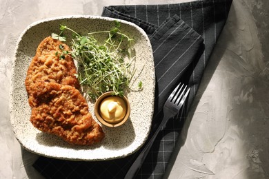 Tasty schnitzels served with sauce and microgreens on grey textured table, top view