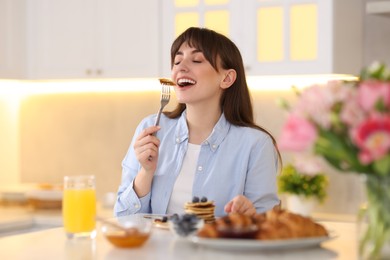 Photo of Smiling woman eating tasty pancakes at breakfast indoors