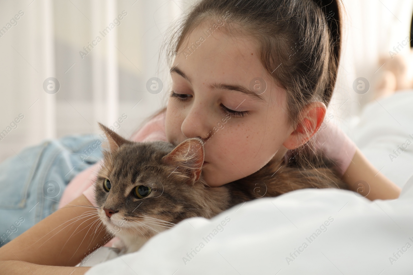 Photo of Cute little girl with cat lying on bed at home. First pet