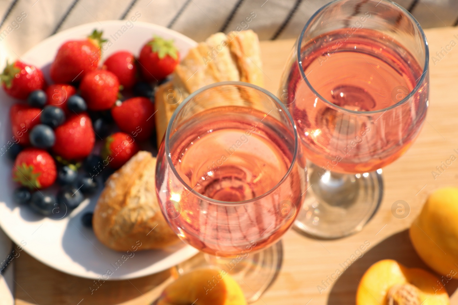 Photo of Glasses of delicious rose wine and food on wooden board, closeup