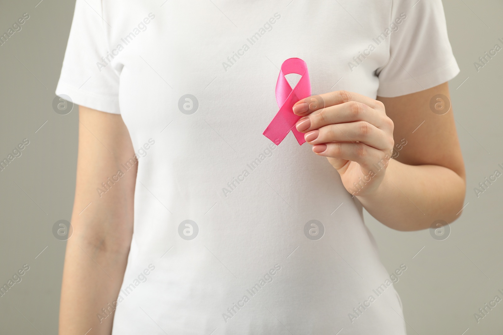 Photo of Woman with pink ribbon on light grey background, closeup. Breast cancer awareness