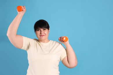 Photo of Happy overweight mature woman doing exercise with dumbbells on light blue background, space for text