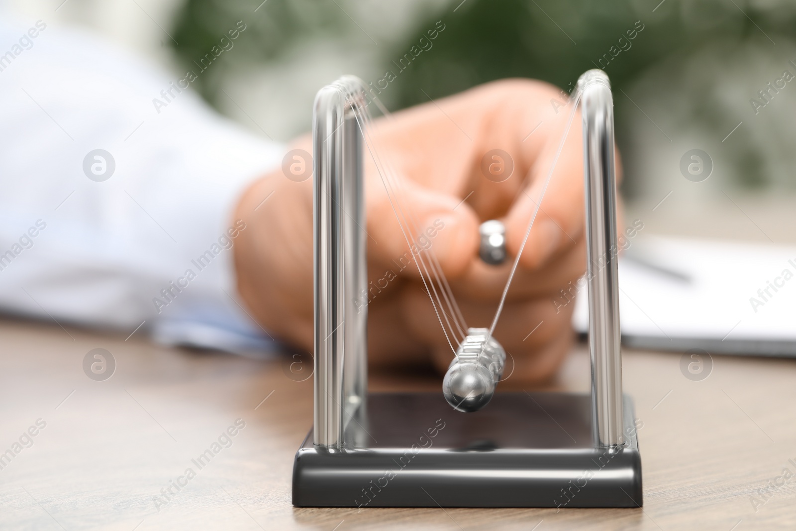 Photo of Man playing with Newton's cradle at table, closeup. Physics law of energy conservation