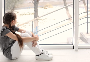 Photo of Lonely little girl near window indoors. Child autism