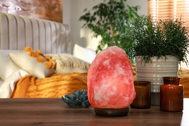 Beautiful Himalayan salt lamp, green plant and decor on wooden table in bedroom, space for text