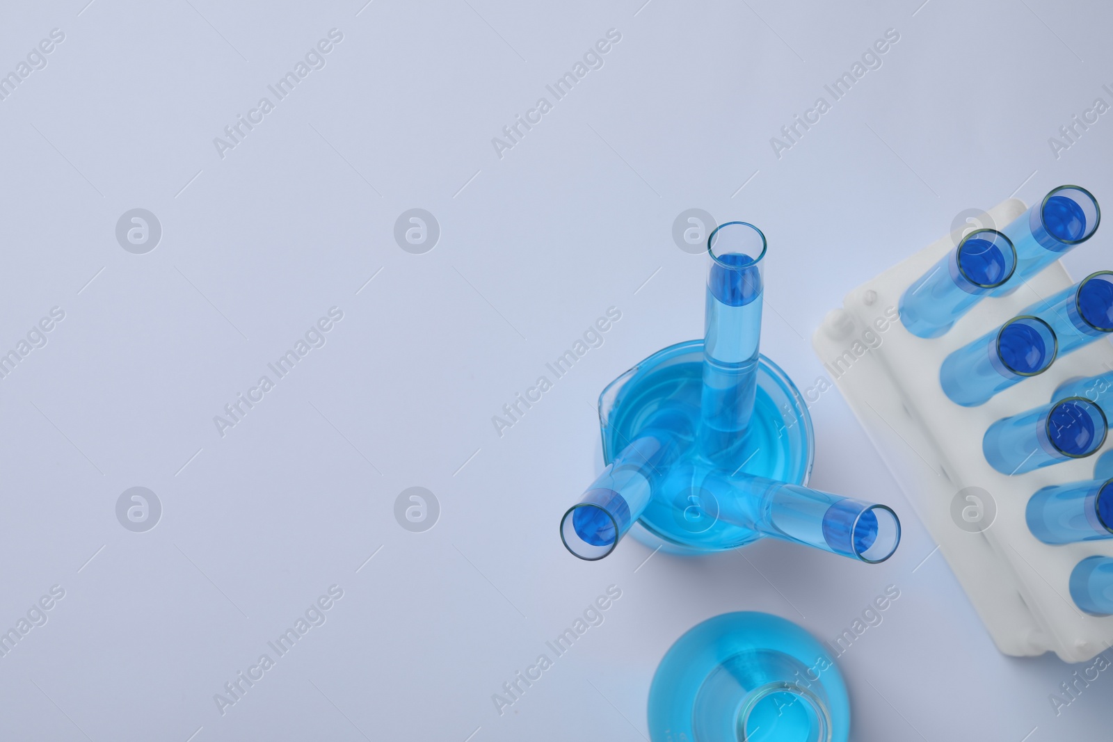 Photo of Laboratory glassware with blue liquid on light grey background, flat lay. Space for text
