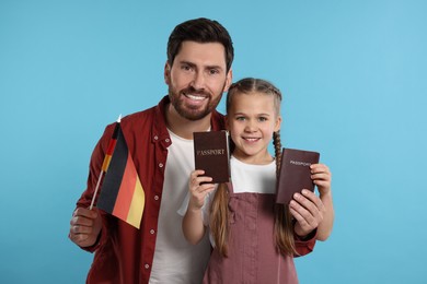 Immigration. Happy man with his daughter holding passports and flag of Germany on light blue background