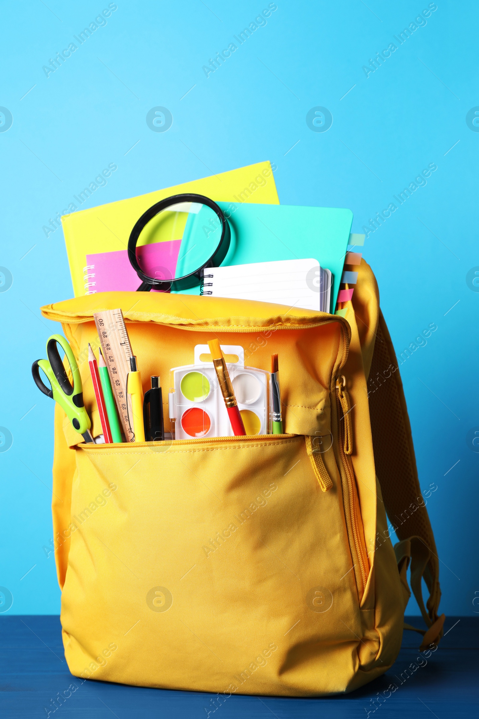 Photo of Yellow backpack and different school stationery on blue wooden table