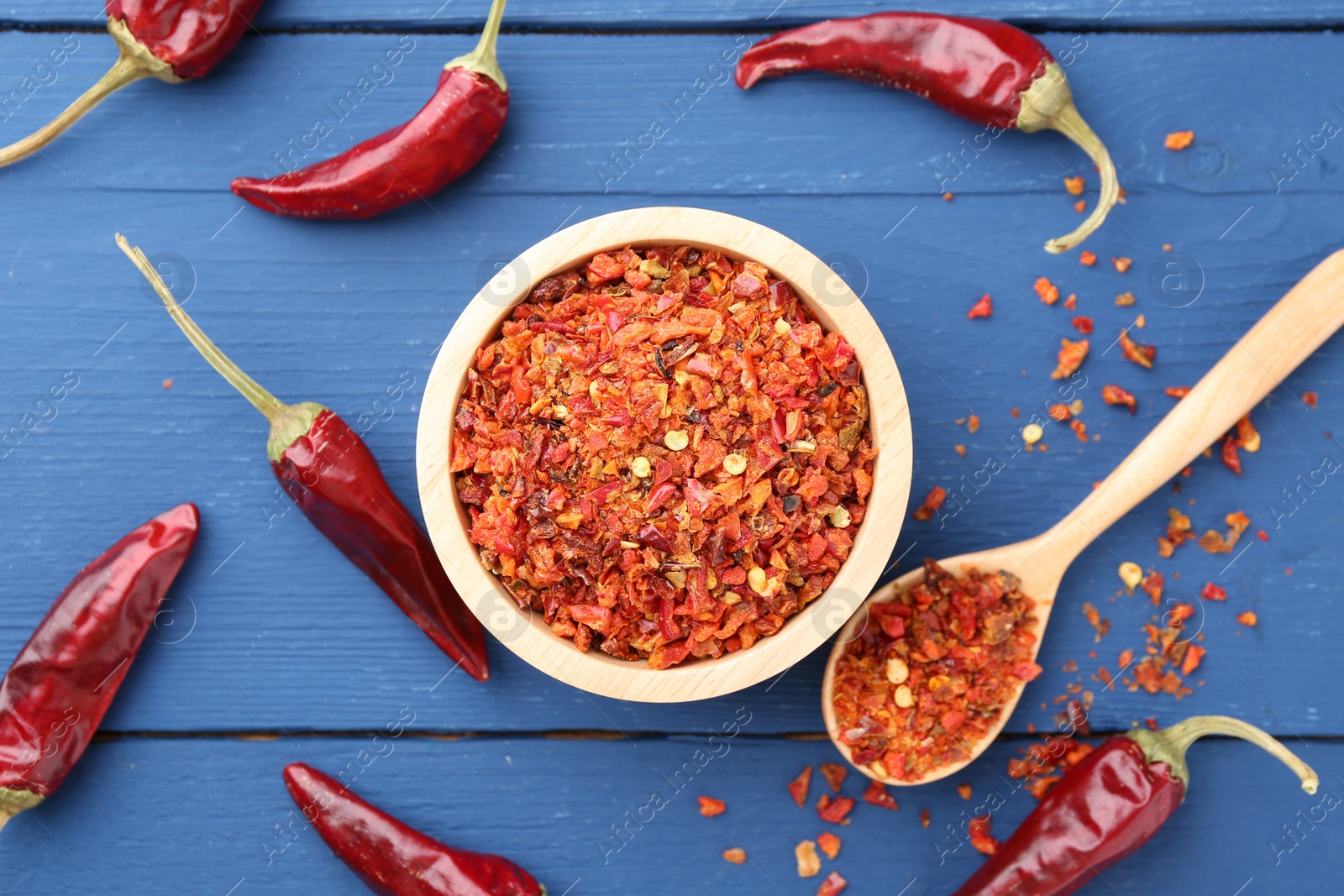 Photo of Chili pepper flakes and pods on blue wooden table, flat lay