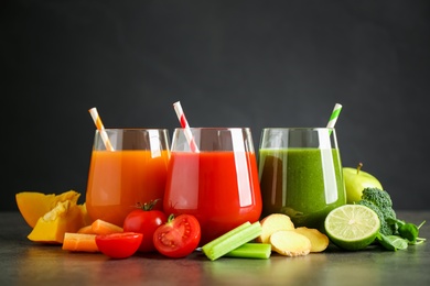 Photo of Different tasty juices and fresh ingredients on grey table against black background