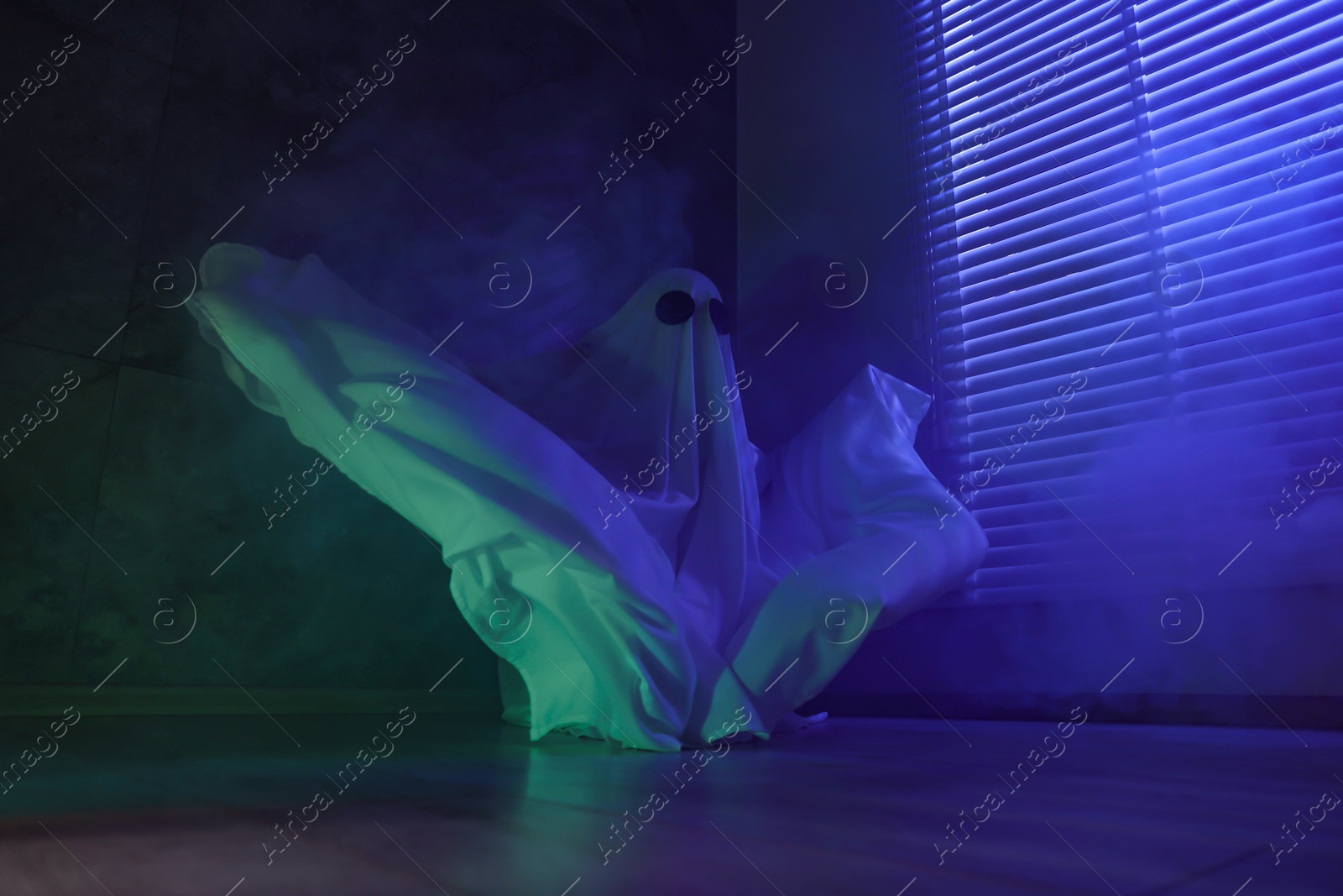 Photo of Creepy ghost. Woman covered with sheet near window in blue light