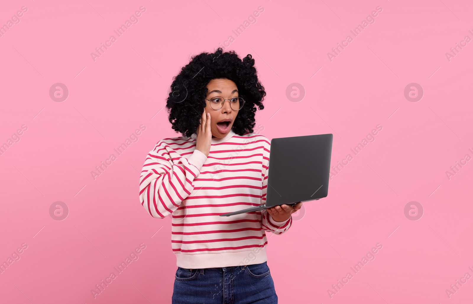 Photo of Emotional young woman with laptop on pink background