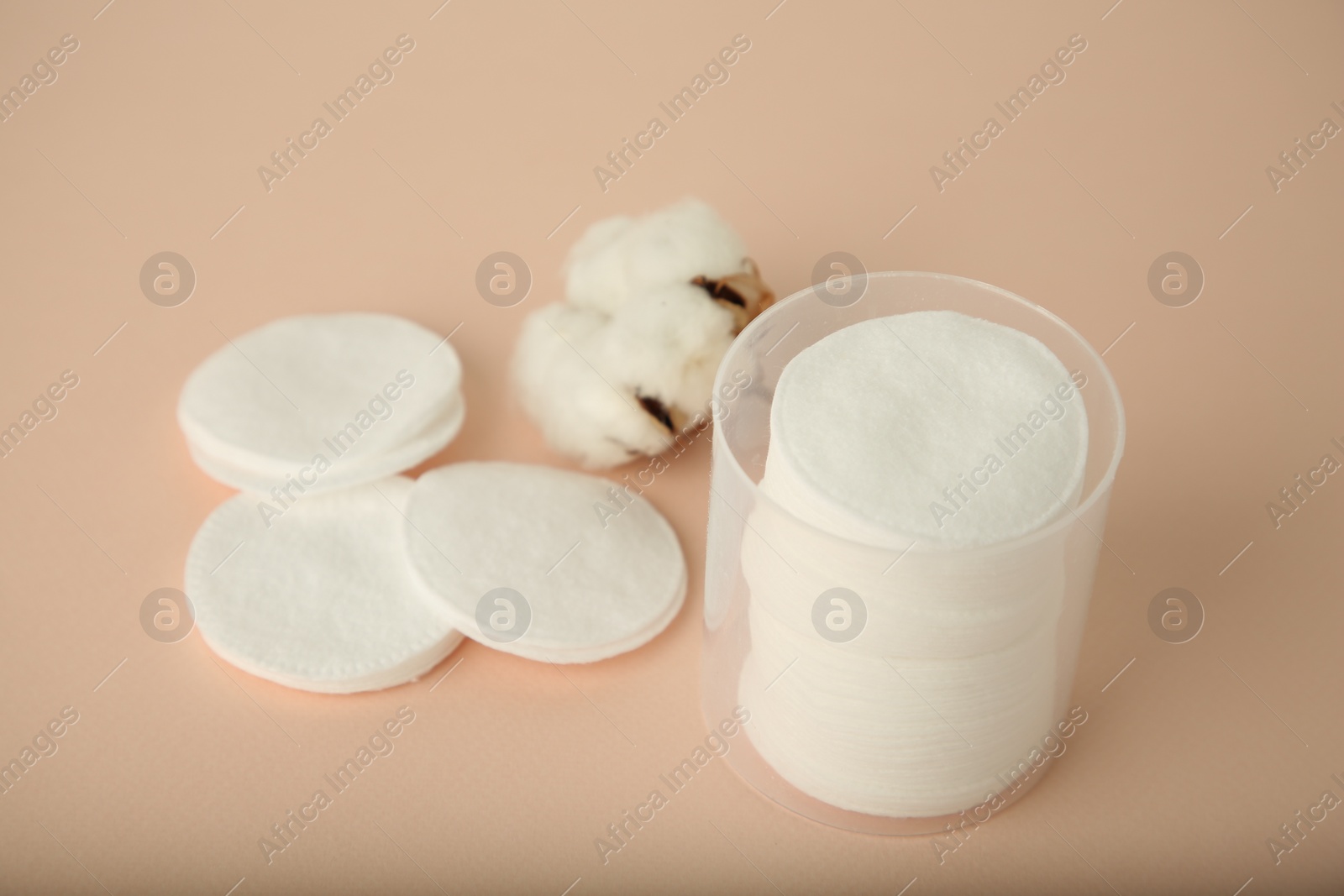 Photo of Container with cotton pads and flower on beige background, closeup