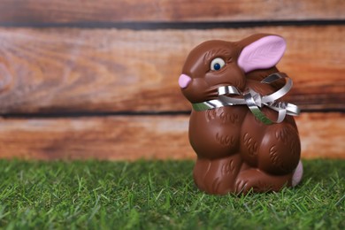 Easter celebration. Cute chocolate bunny on grass against wooden background. Space for text