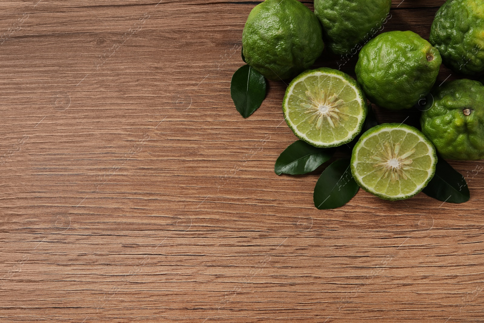 Photo of Fresh ripe bergamot fruits with green leaves on wooden table, flat lay. Space for text