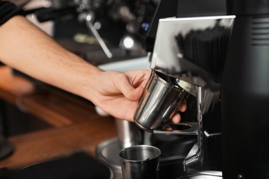 Photo of Barista with metal cup using coffee grinding machine in cafe, closeup