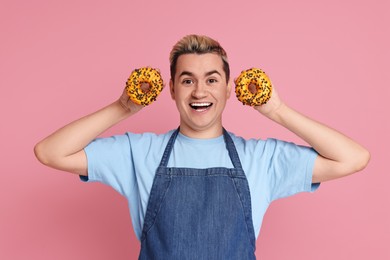 Photo of Portrait of happy confectioner holding donuts on pink background