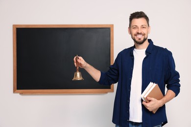 Photo of Teacher with school bell near black chalkboard indoors. Space for text