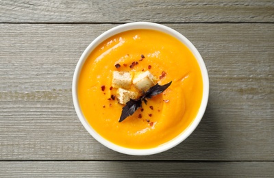 Delicious pumpkin soup in bowl on wooden table, top view