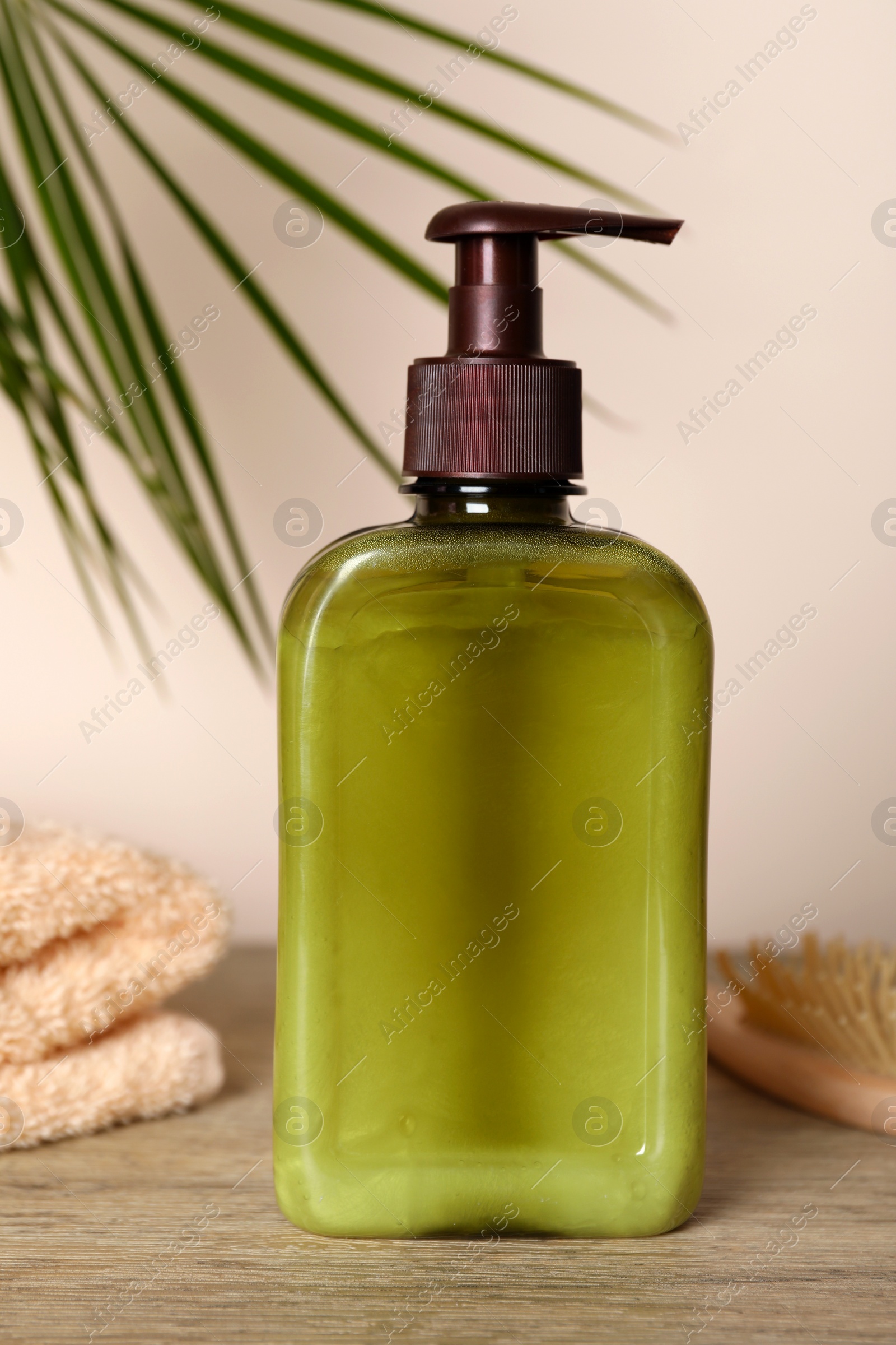 Photo of Bottle of shampoo on wooden table near beige wall