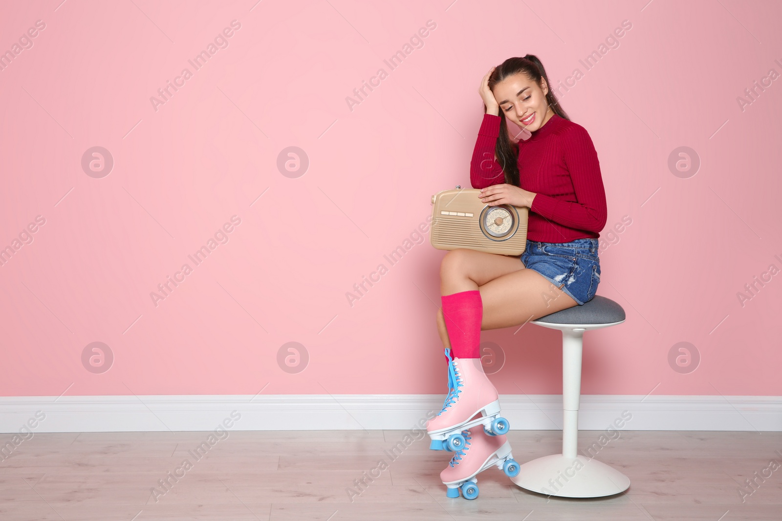 Photo of Young woman with roller skates and retro radio sitting on chair near color wall. Space for text