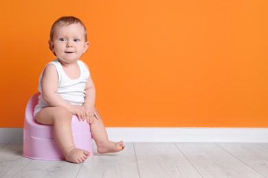 Photo of Little child sitting on baby potty near orange wall. Space for text