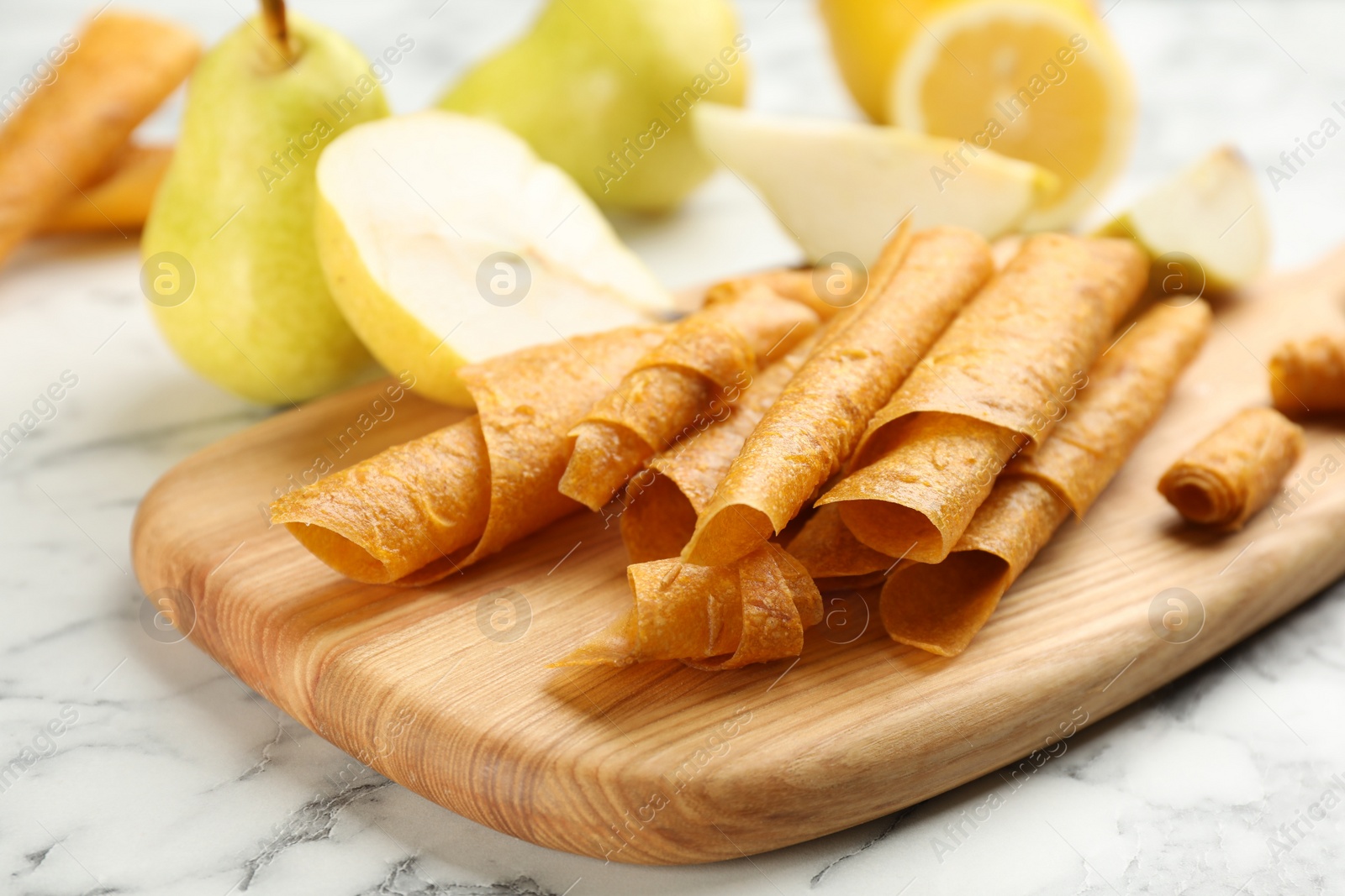 Photo of Delicious fruit leather rolls on white marble table, closeup