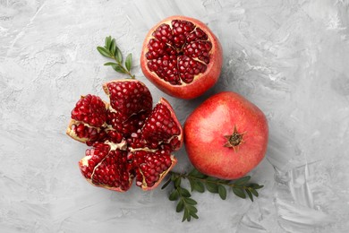 Photo of Fresh pomegranates and green leaves on grey textured table, flat lay