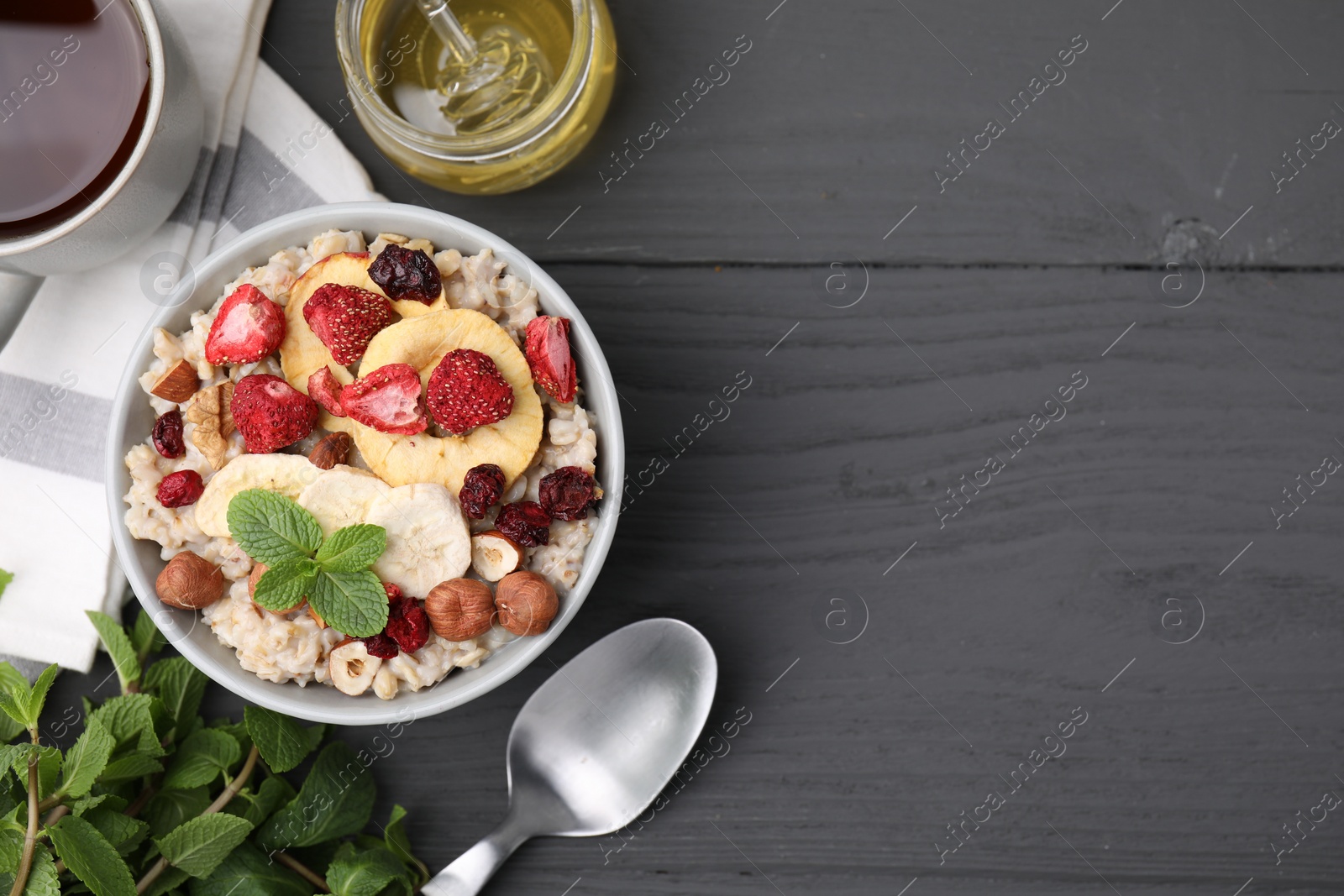 Photo of Oatmeal with freeze dried fruits, nuts and mint on grey wooden table, flat lay. Space for text