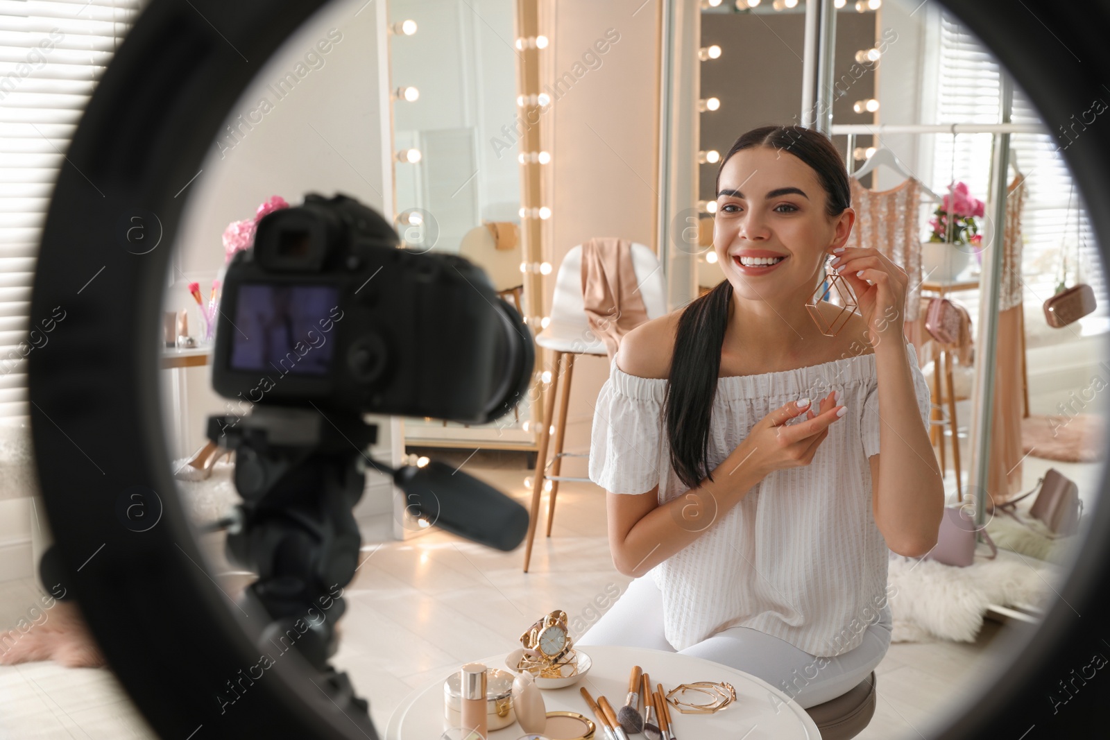 Photo of Blogger with beautiful earring recording video in dressing room at home, view through ring lamp