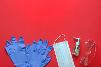 Photo of Flat lay composition with medical gloves, mask and hand sanitizer on red background. Space for text