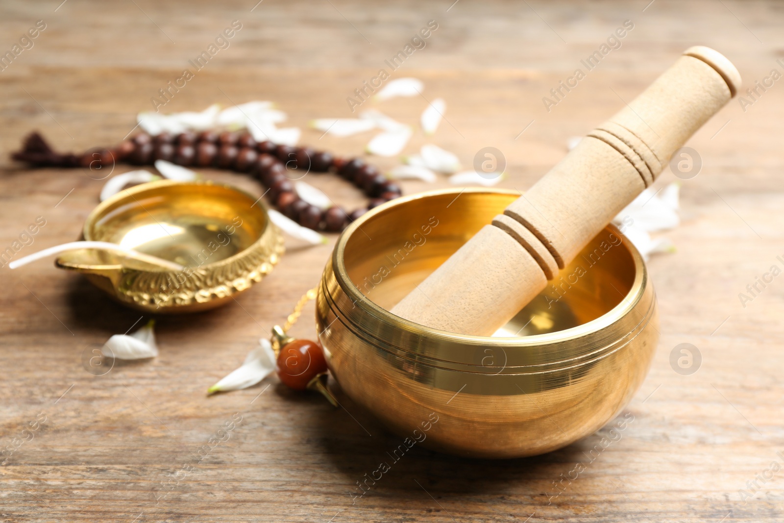 Photo of Composition with golden singing bowl and mallet on wooden table. Sound healing