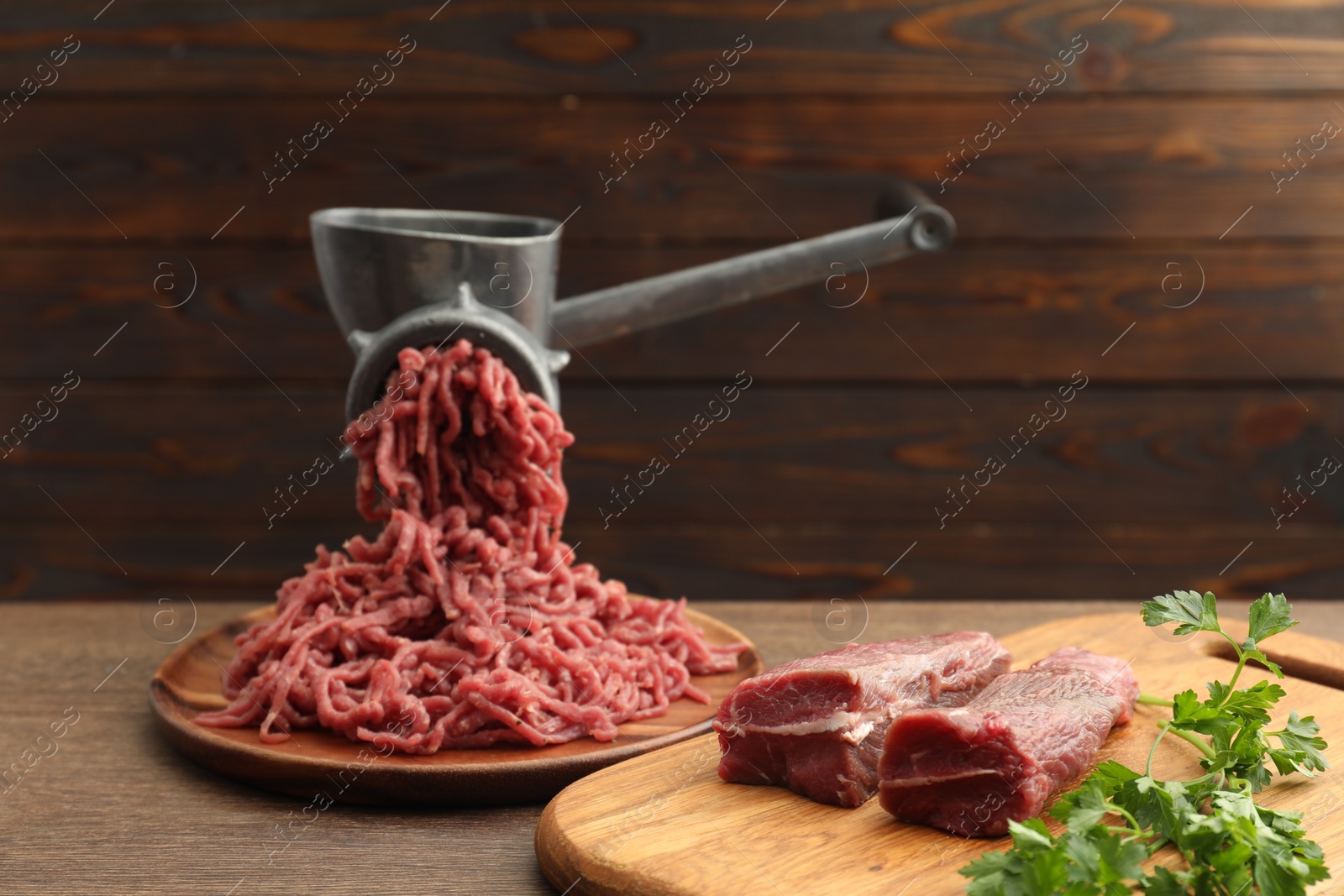 Photo of Manual meat grinder with beef and parsley on wooden table